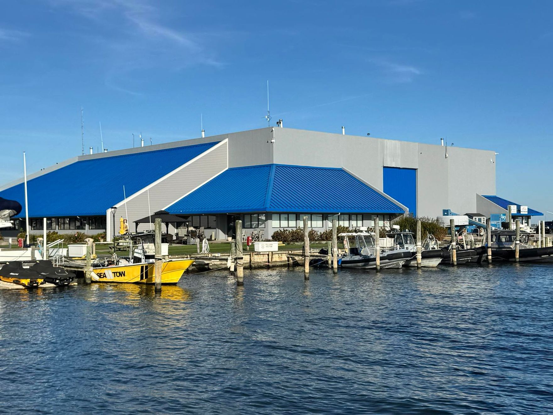 Blue-roofed waterfront building with docks and boats on calm water under a clear sky