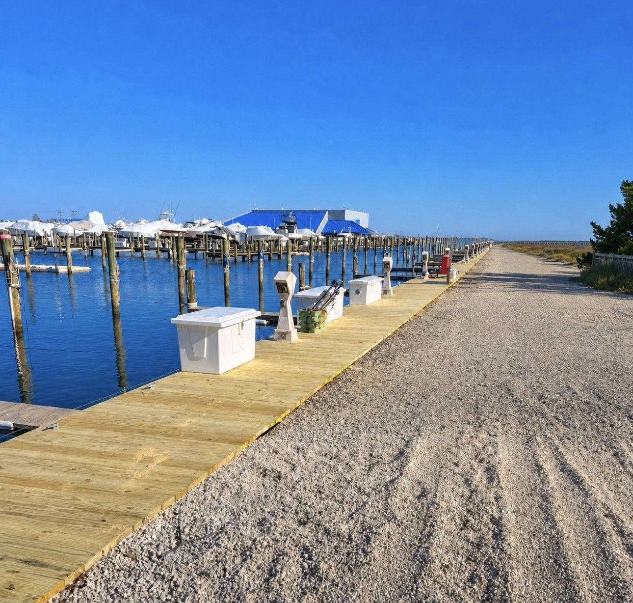 Wooden dock beside a calm blue marina, with a gravel path and clear sky.