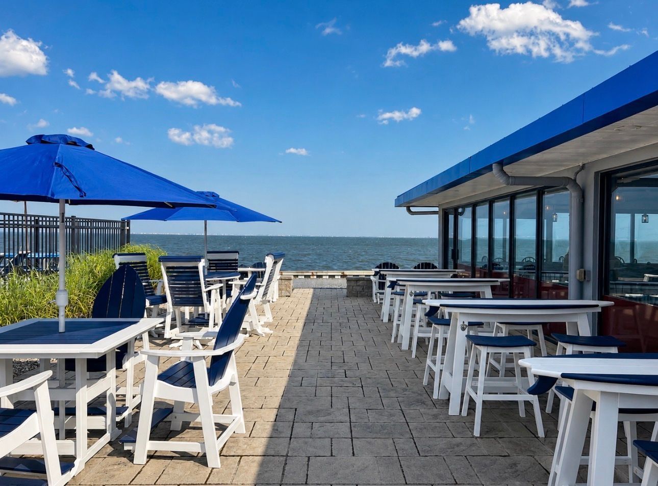 Seaside café terrace with white tables and blue umbrellas overlooking the ocean
