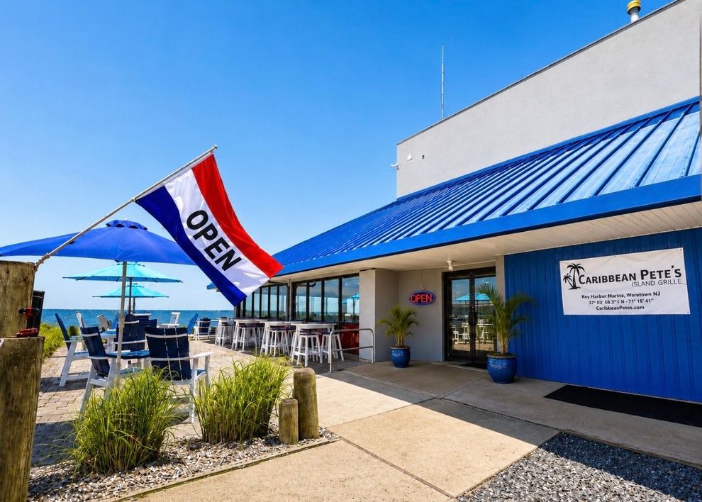 Outdoor storefront with a blue roof, open flag, and patio seating under a bright sky
