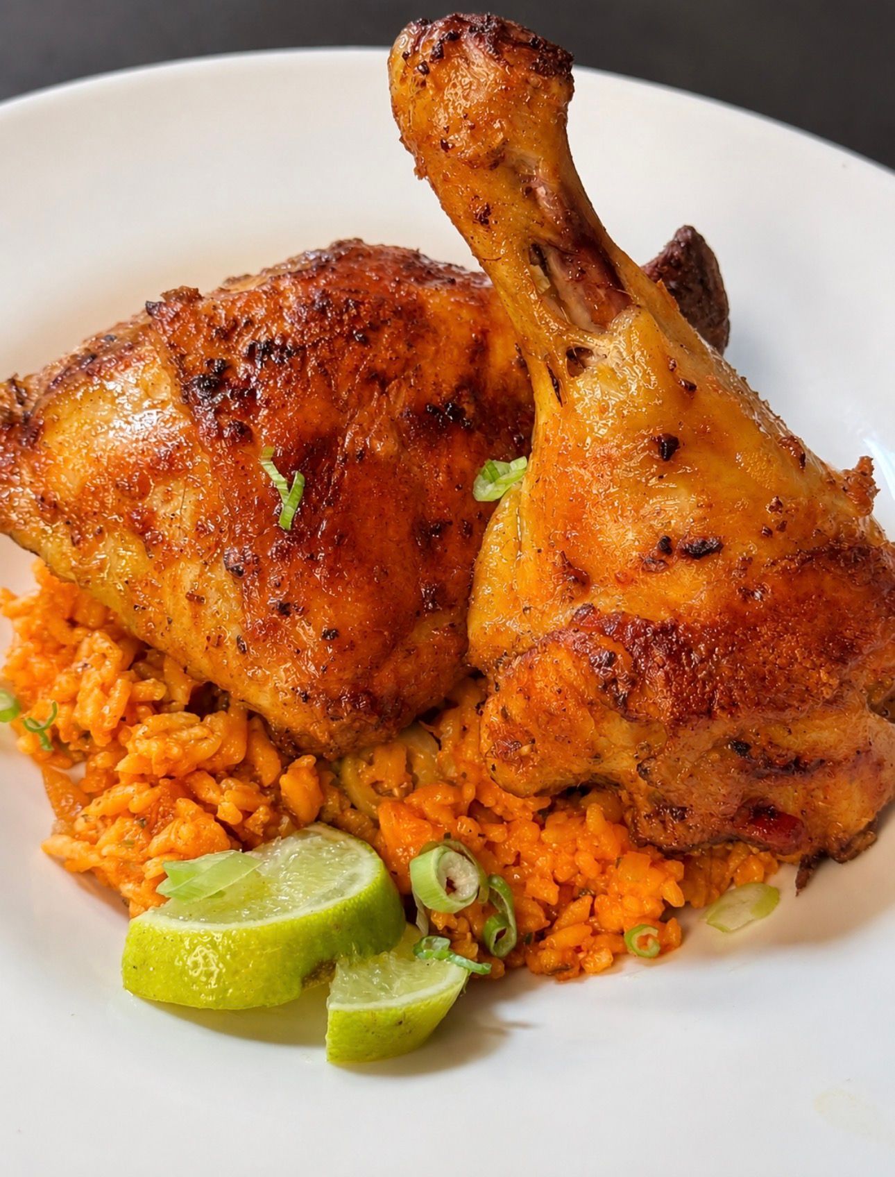Seasoned roasted chicken legs over red rice with lime wedges on a white plate