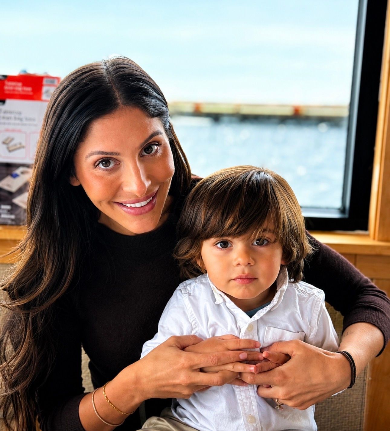Woman holding a child by a window, both facing the camera and smiling