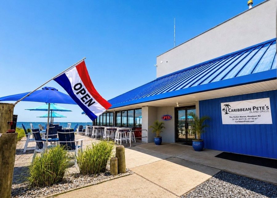 Cafe storefront with blue awning and an open flag outside on a sunny day