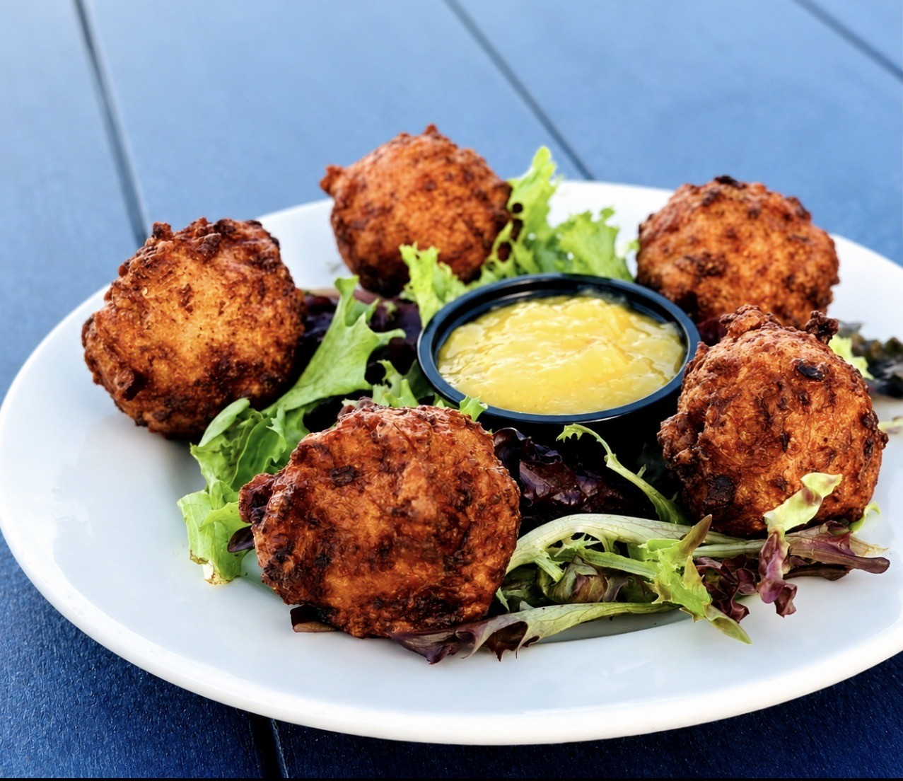 Plate of crispy fried bites on lettuce with a yellow dipping sauce in the center