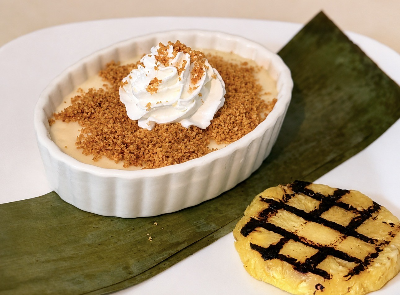 Dessert trio on a banana leaf: custard in a ramekin, whipped cream-topped dessert, and a grilled yellow cake square
