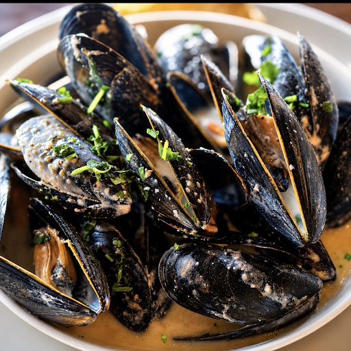 Bowl of cooked mussels in dark shells topped with chopped herbs