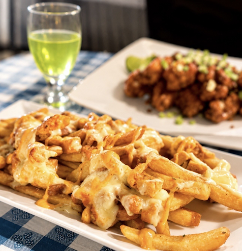 Cheesy fries and fried chicken on a table with a green drink in the background