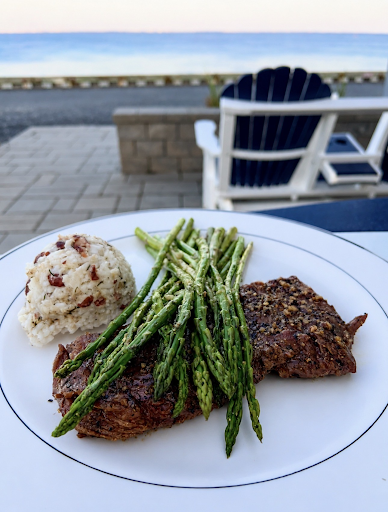 Plated steak with asparagus and rice on a table by the ocean at sunset