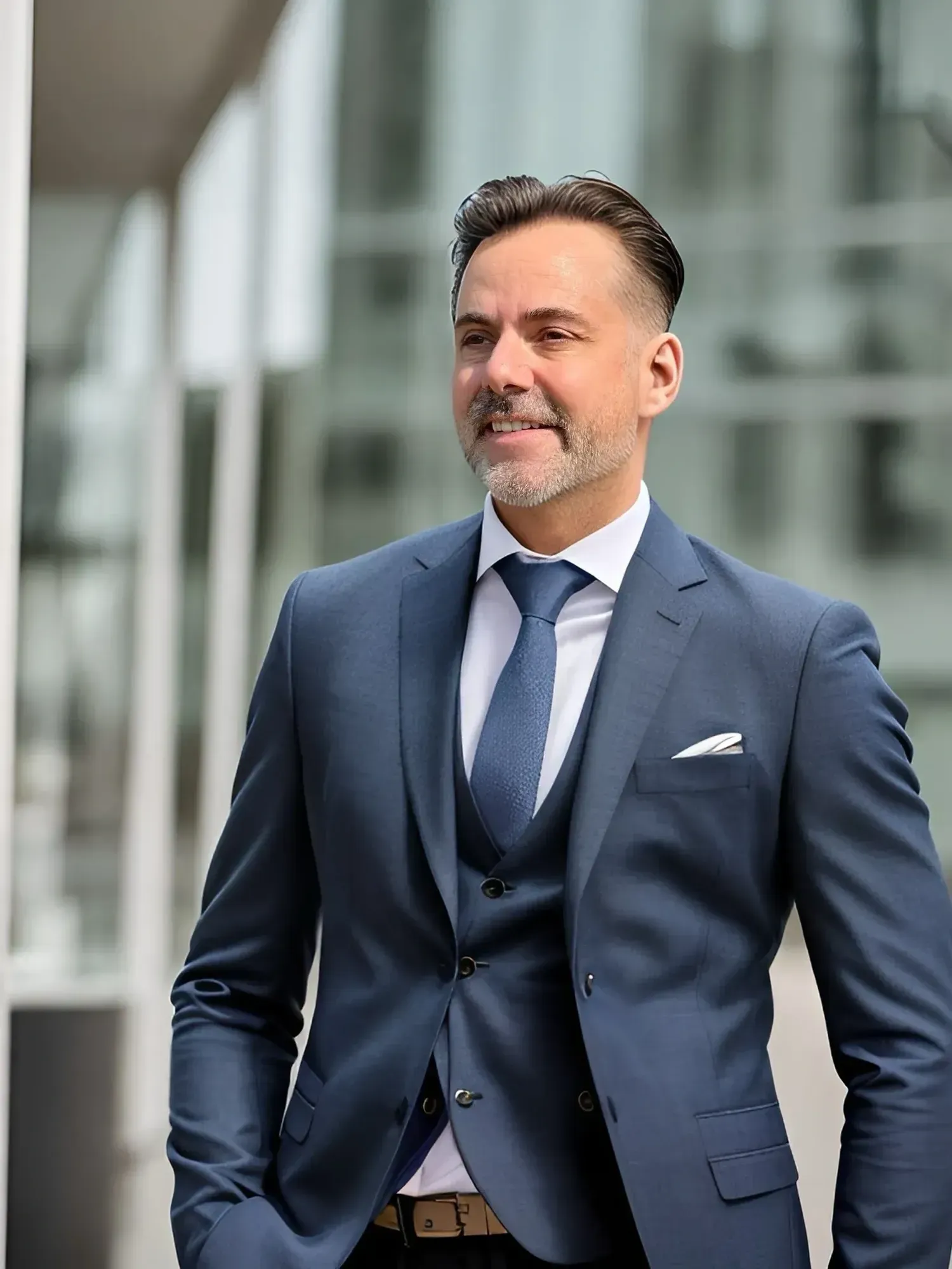 A man in a blue suit and tie is standing in front of a building.