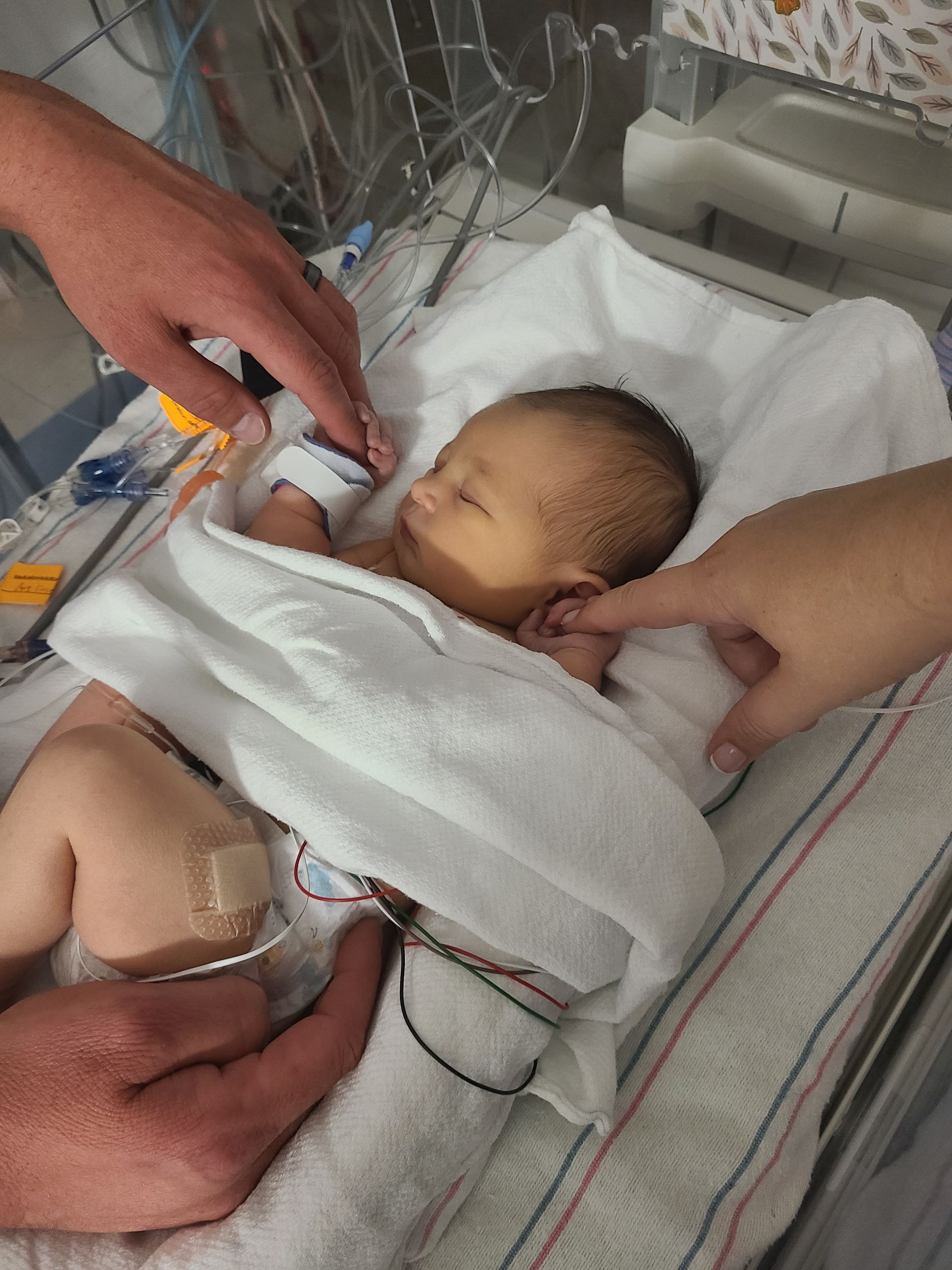 A baby wrapped in a white blanket is being held by two people.