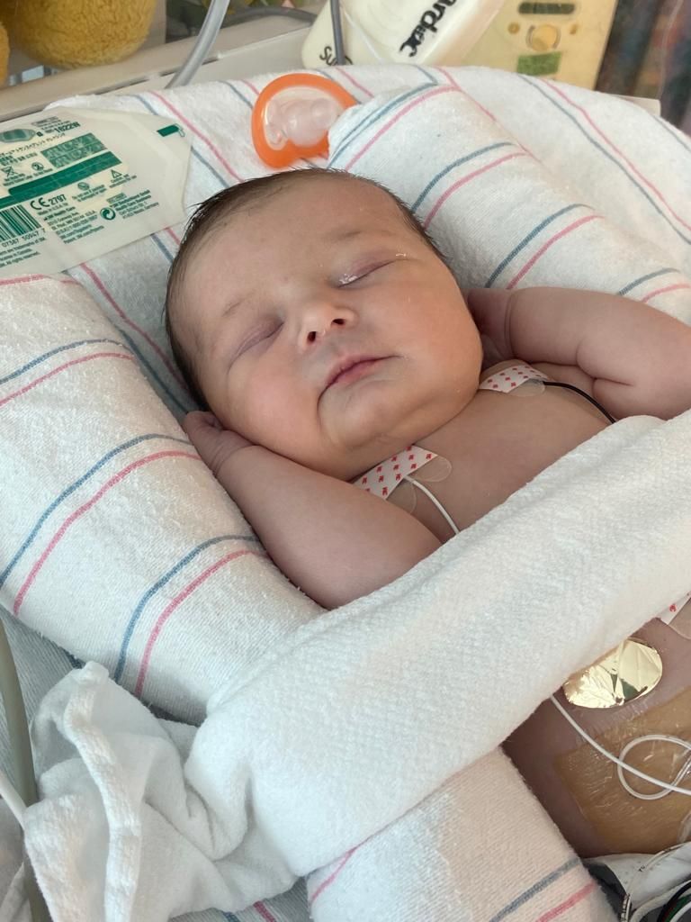 A newborn baby is sleeping in a hospital bed.