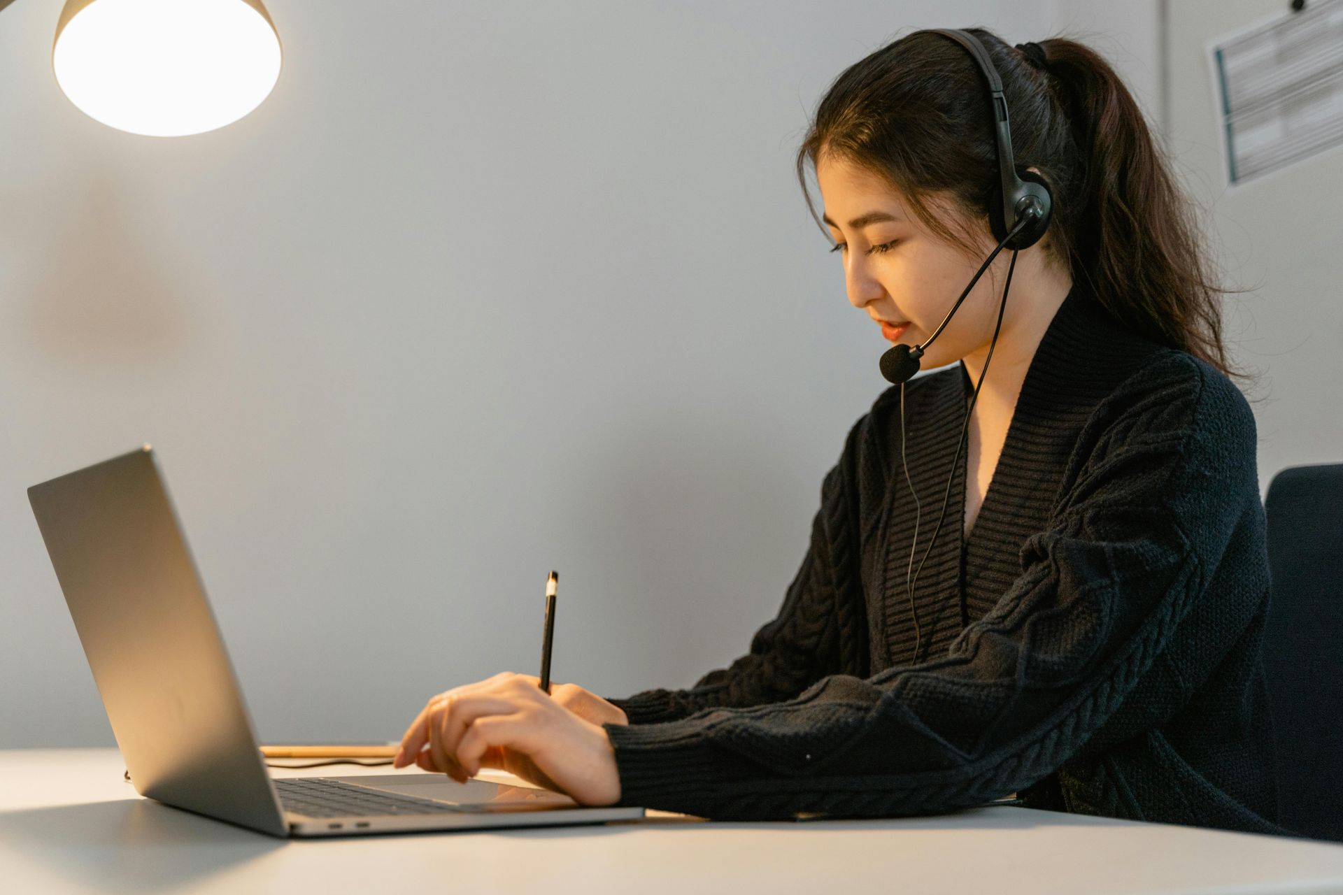 A woman wearing headphones is sitting at a desk using a laptop computer.