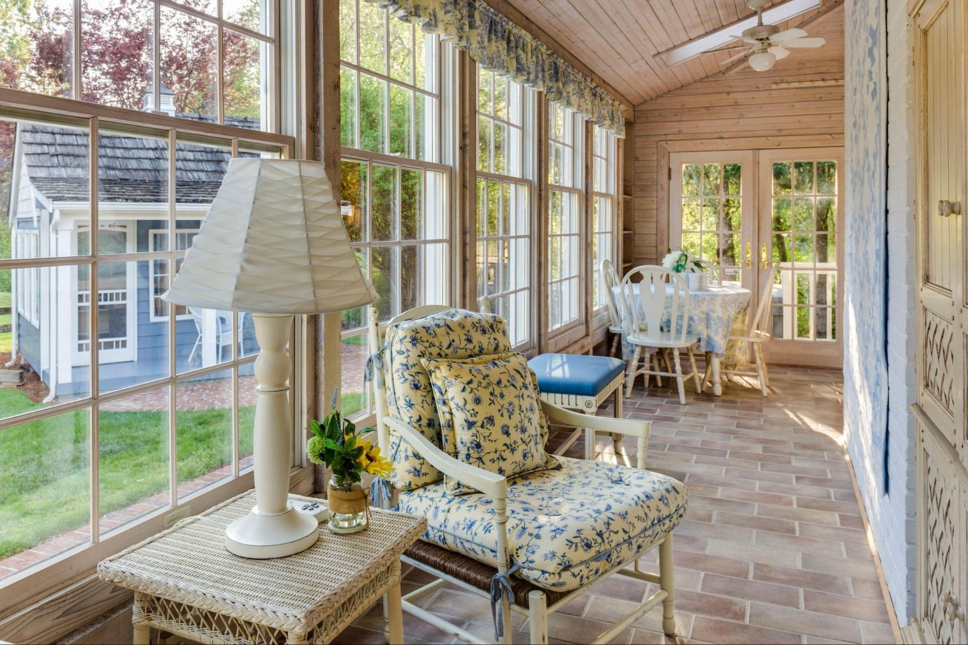 A sun room with a chair , table , lamp and lots of windows.