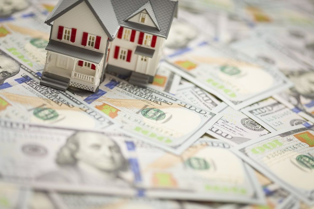 A model house is sitting on top of a pile of money.