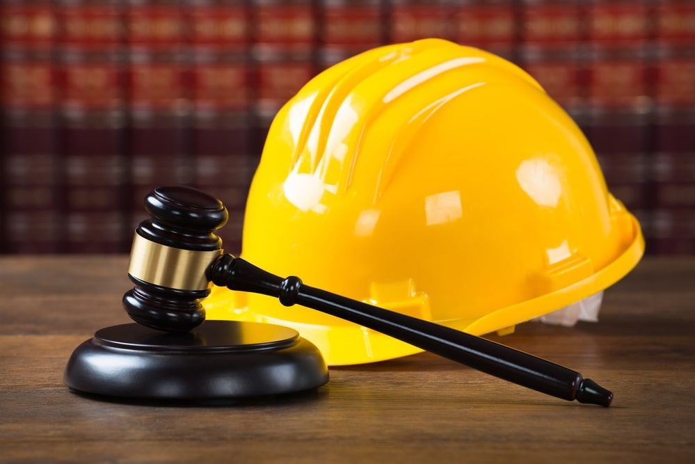 A yellow hard hat and a judge 's gavel on a wooden table.