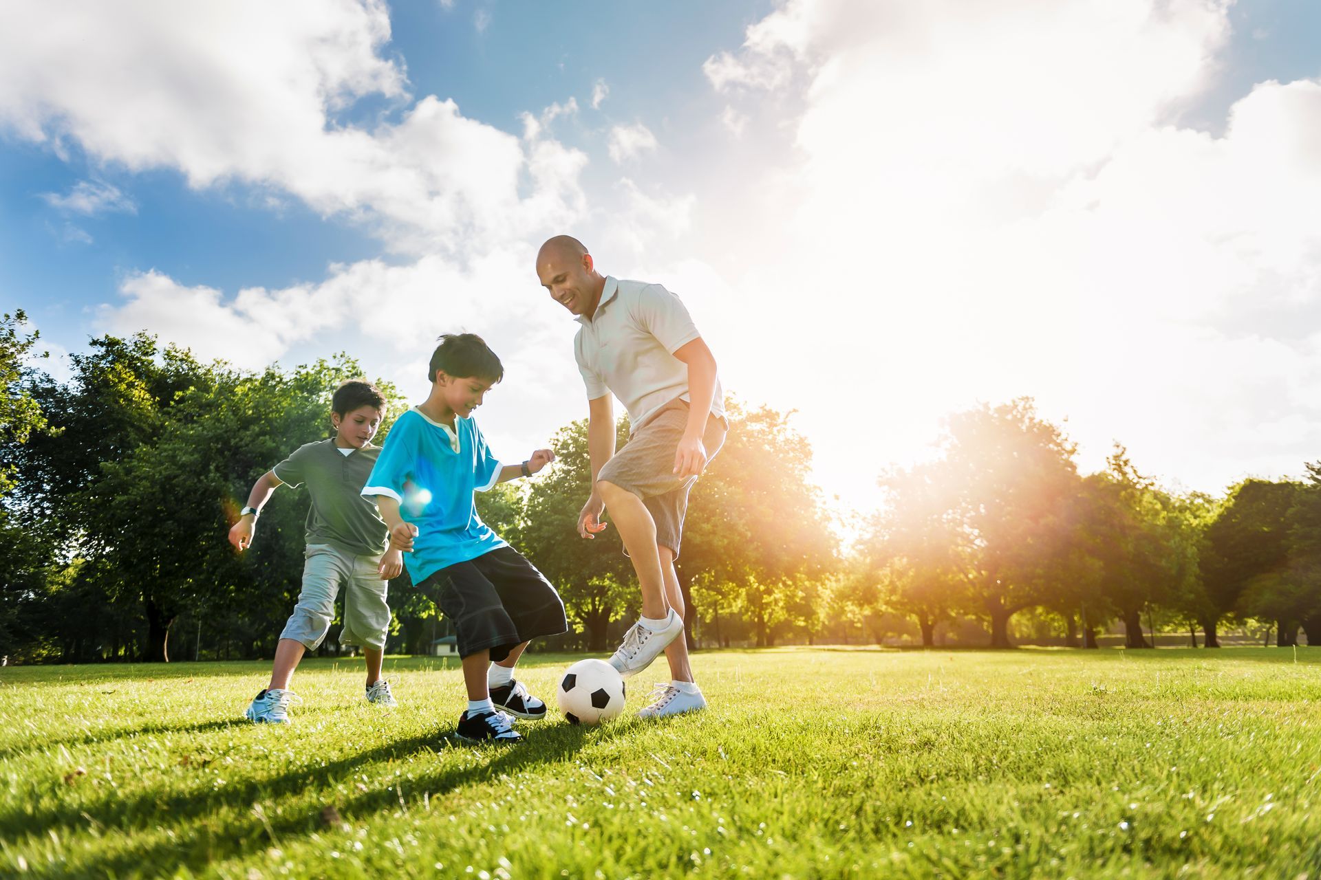 Dad and sons playing soccer at a park