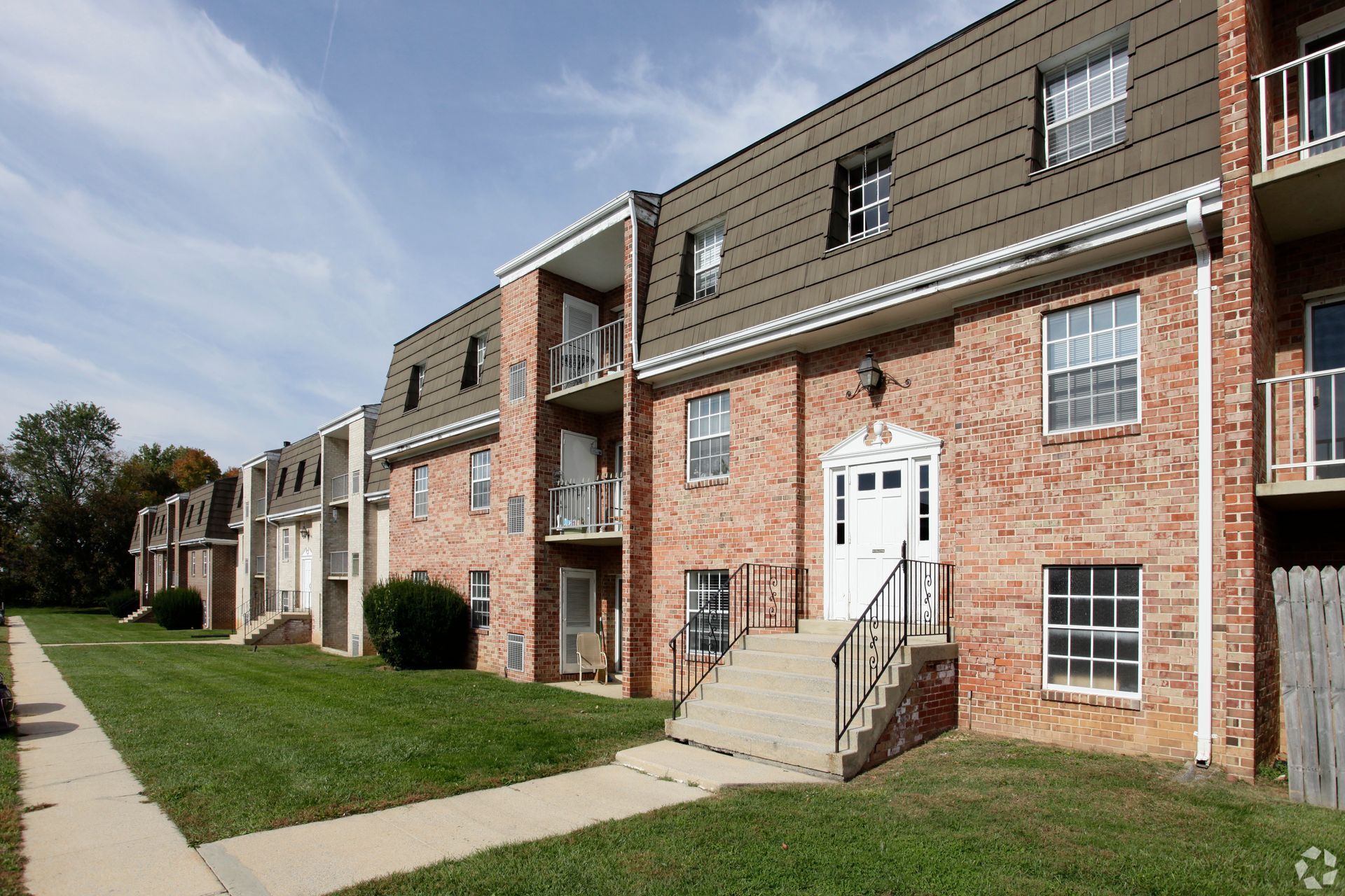 Apartment complex with brick exteriors and a parking lot. Cloudy sky, trees in the background.
