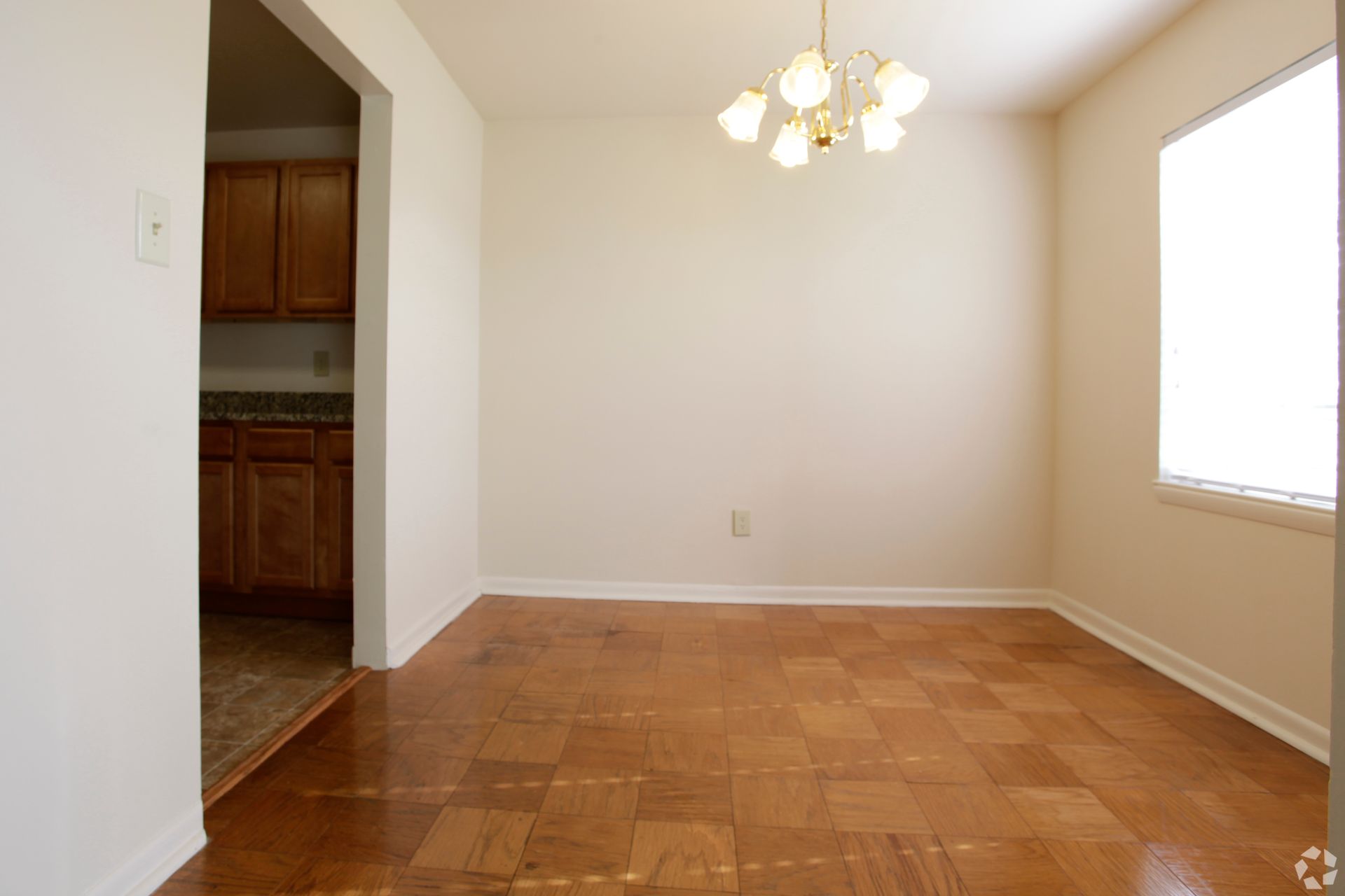 Empty dining room with wood floor, small chandelier, and kitchen entrance.