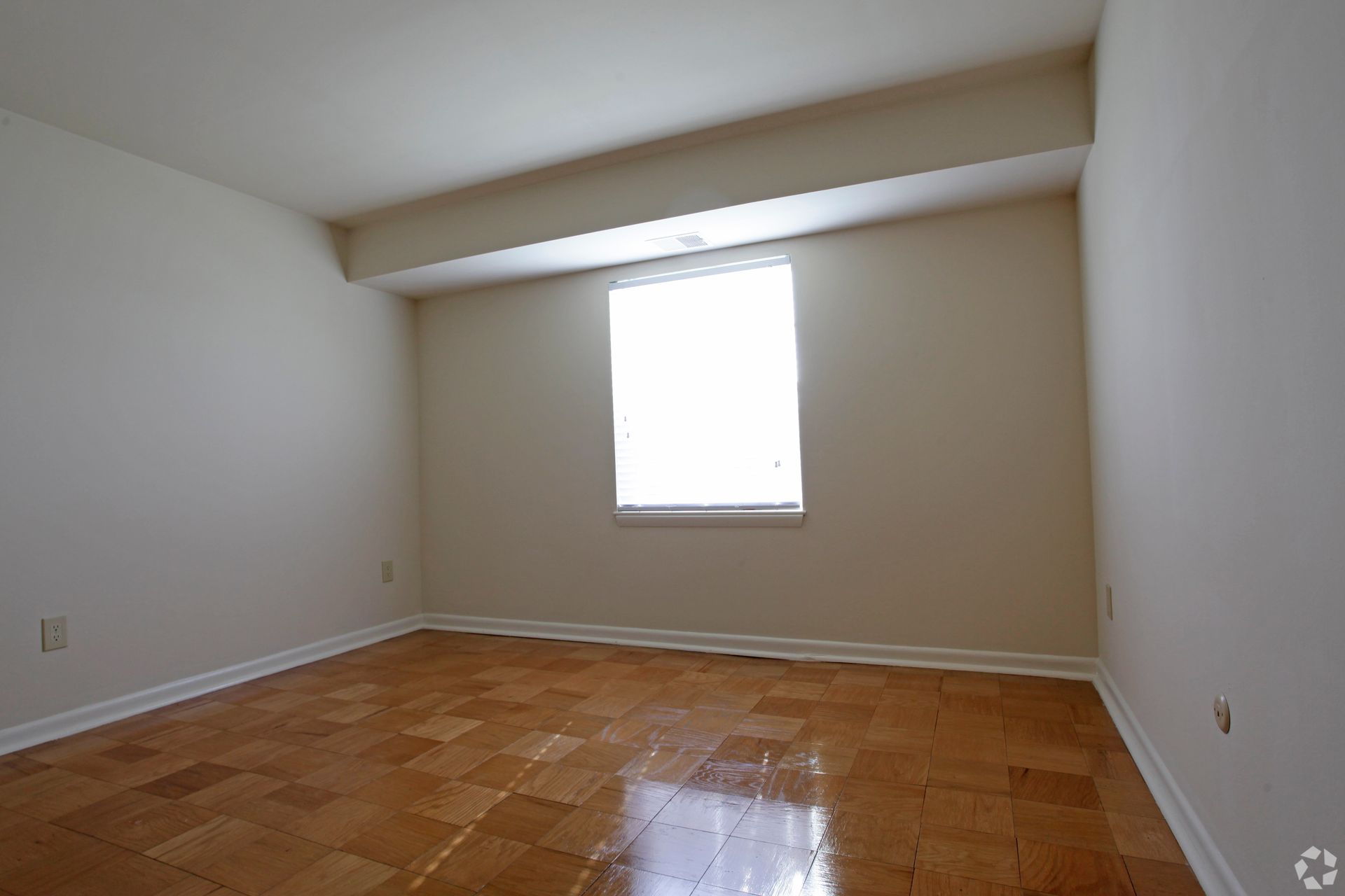 Empty room with wooden floor, window, and off-white walls.