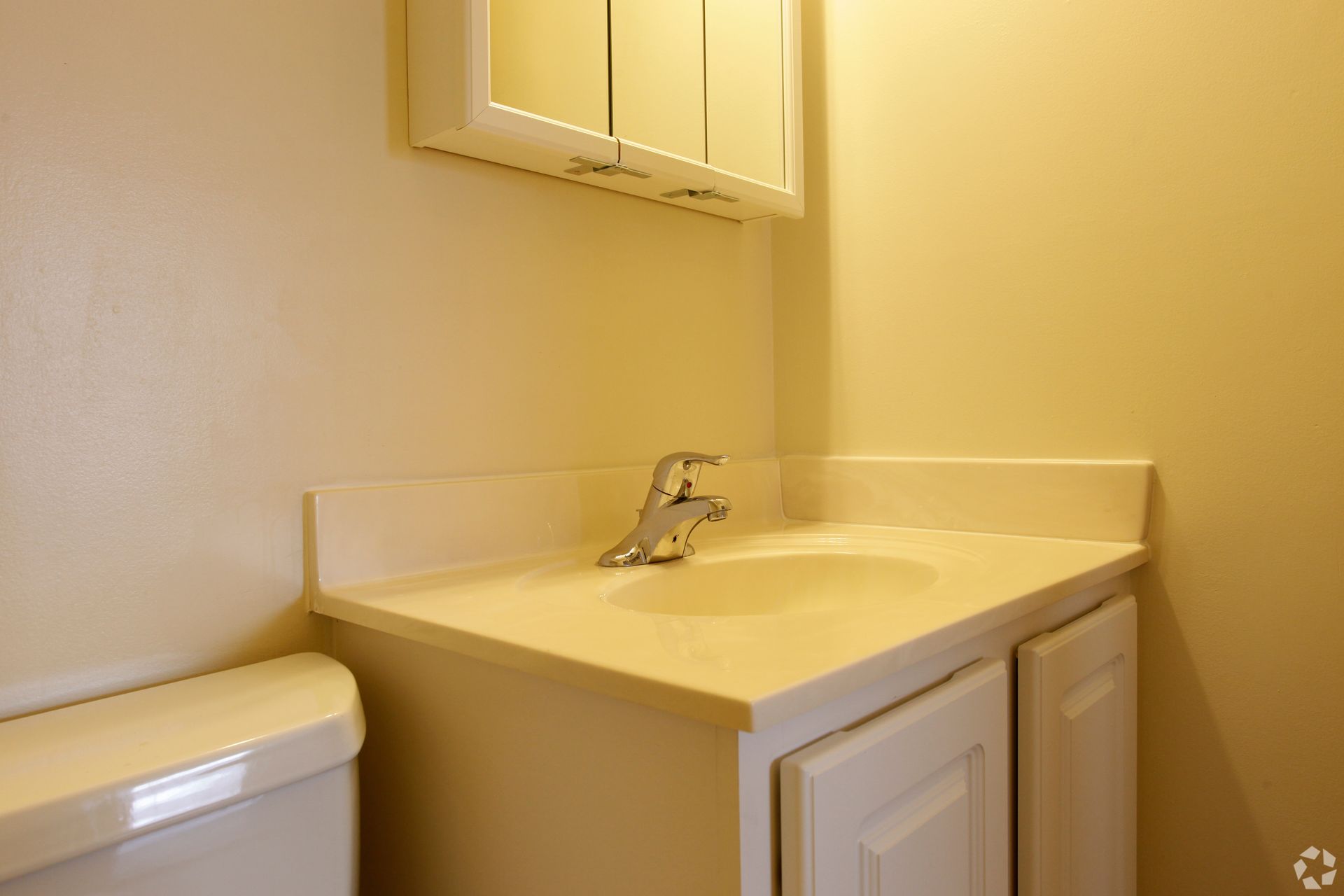 Bathroom with white sink, cabinet, and toilet. A chrome faucet and medicine cabinet are visible.