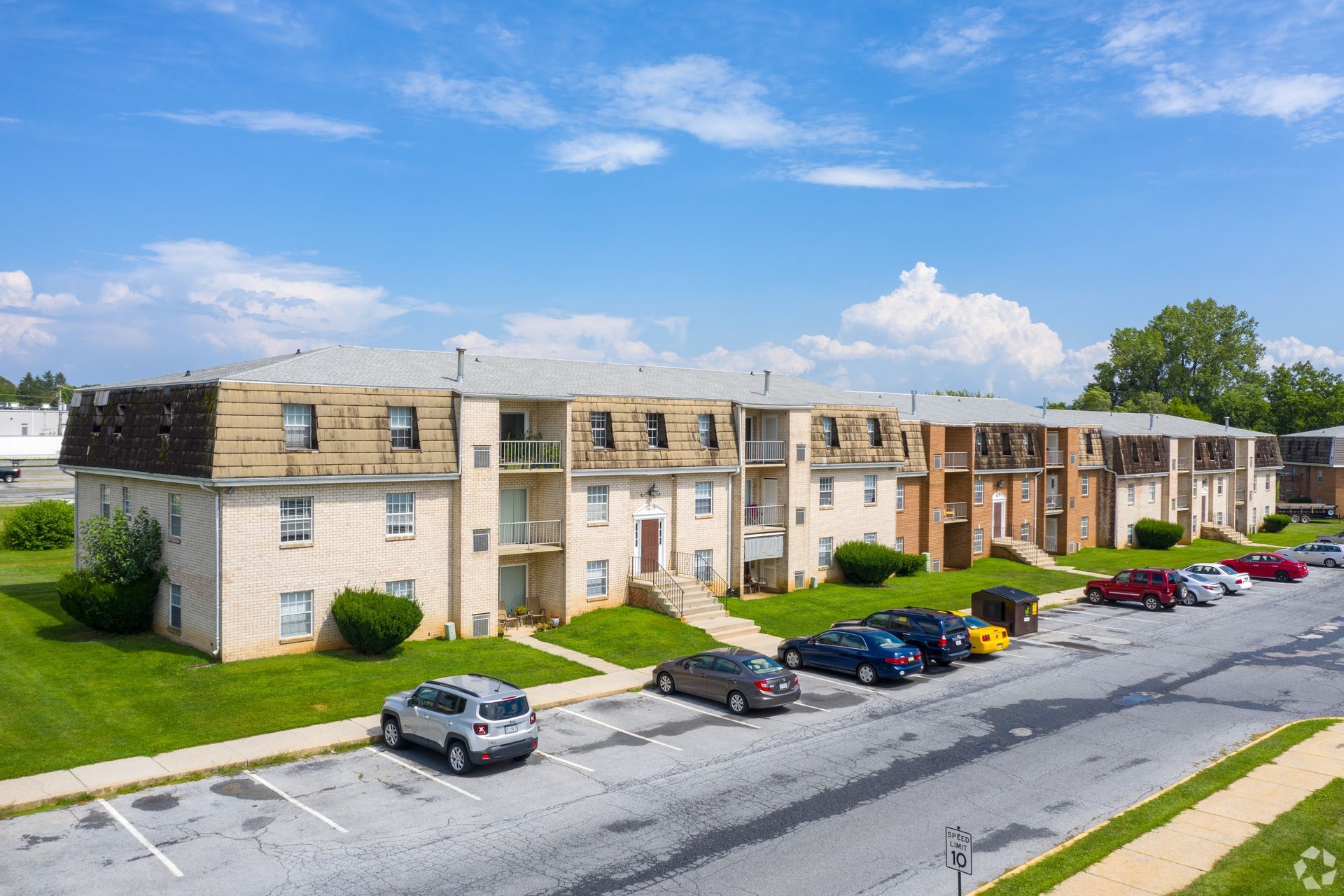 Apartment complex with parked cars, green lawn, and blue sky.