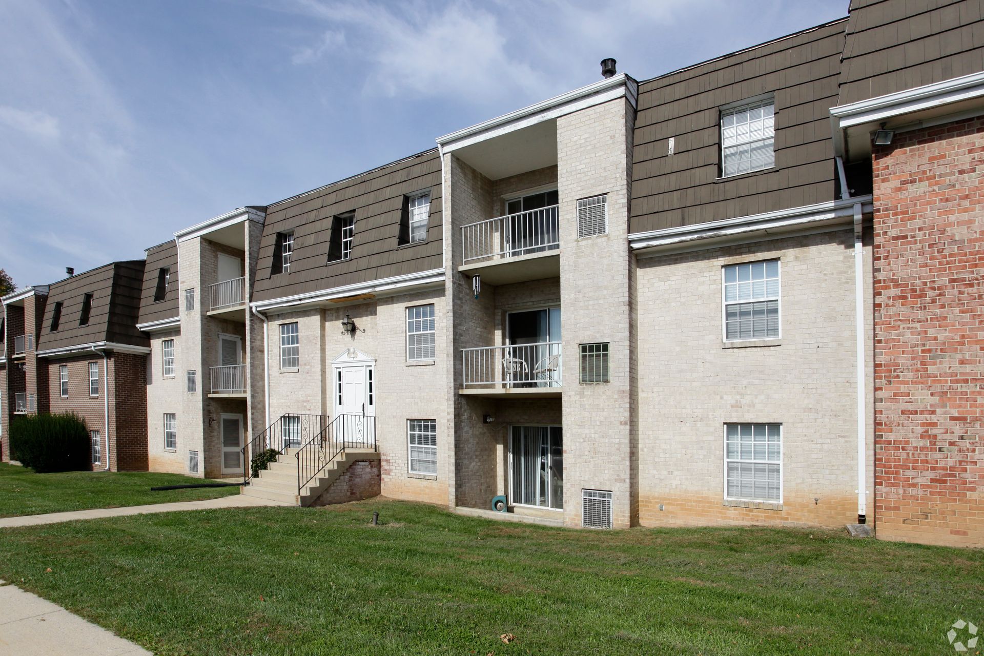 Apartment building with beige brick and brown roof, balconies, and green grass lawn.