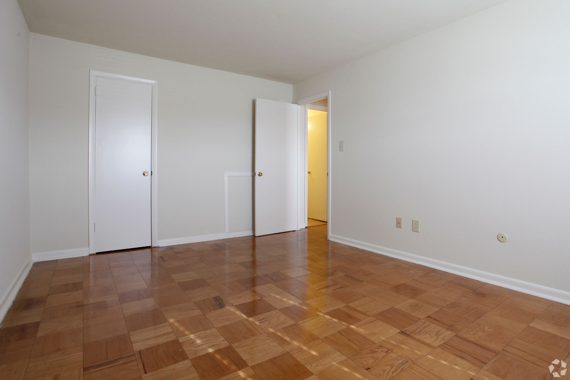 Empty room with hardwood floors, white walls, two closed doors, and a doorway.