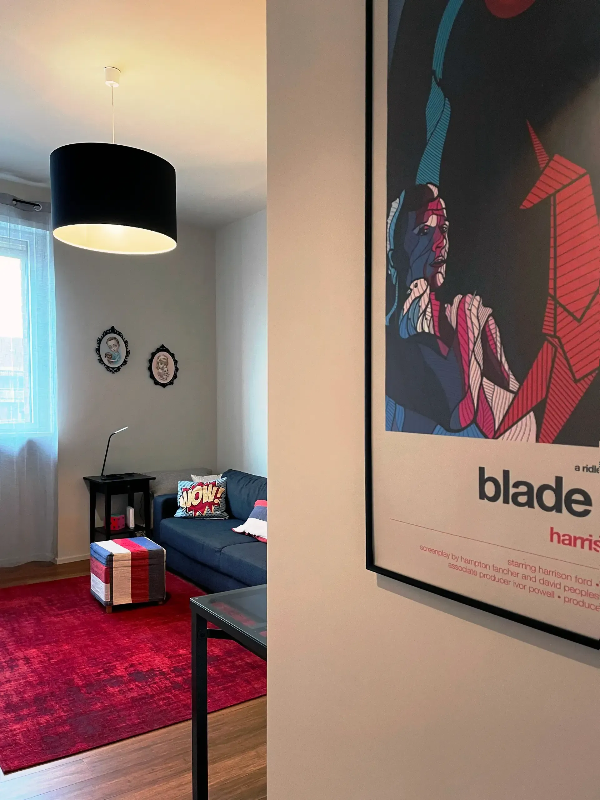 Soggiorno con tappeto rosso, divano blu, lampada nera e un poster di Blade Runner.
