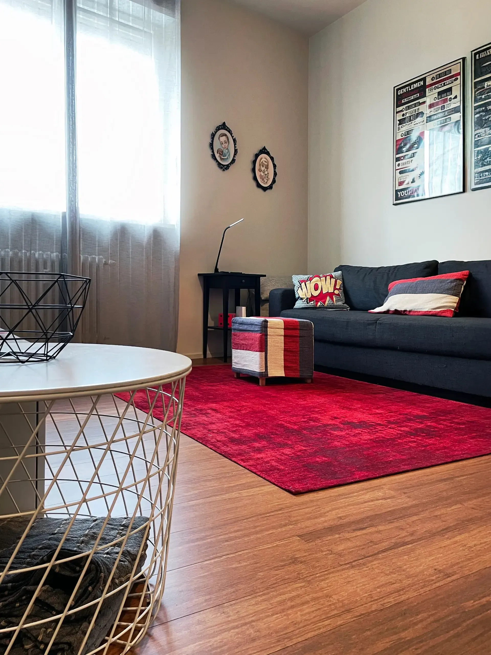 Soggiorno con tappeto rosso, divano grigio, tavolino da caffè e quadri incorniciati.