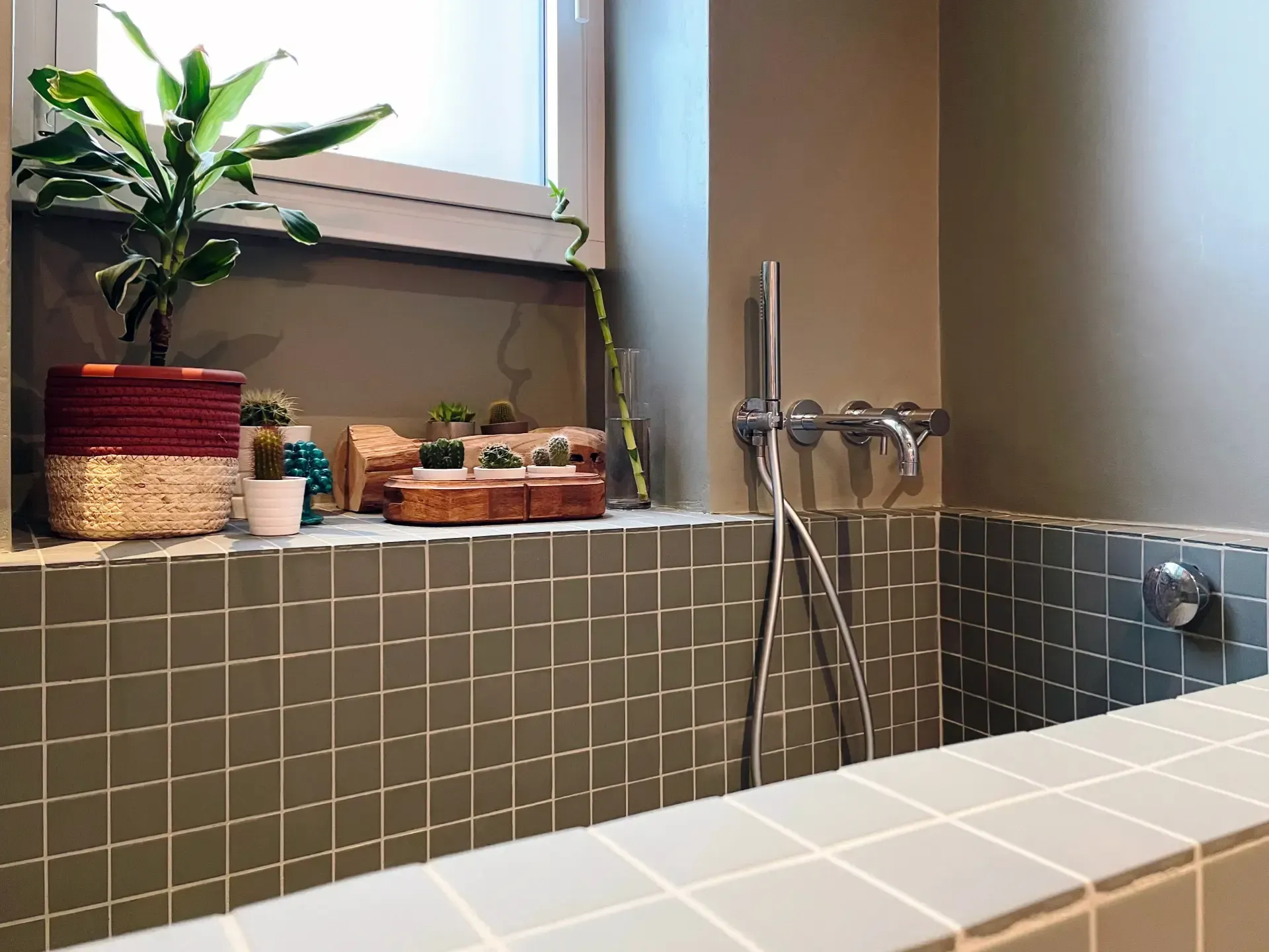 Bagno con piastrelle grigie, piante sul davanzale e sanitari cromati.