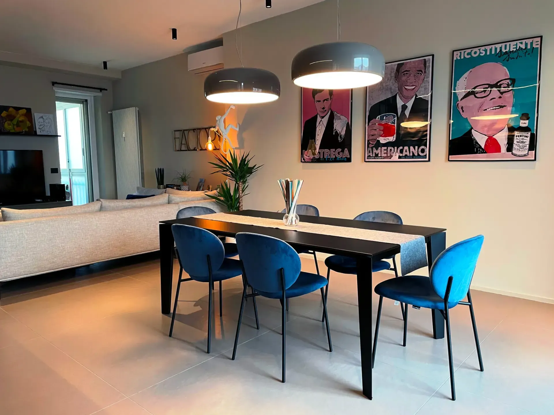 Sala da pranzo con tavolo nero, sedie blu e pop art alla parete.