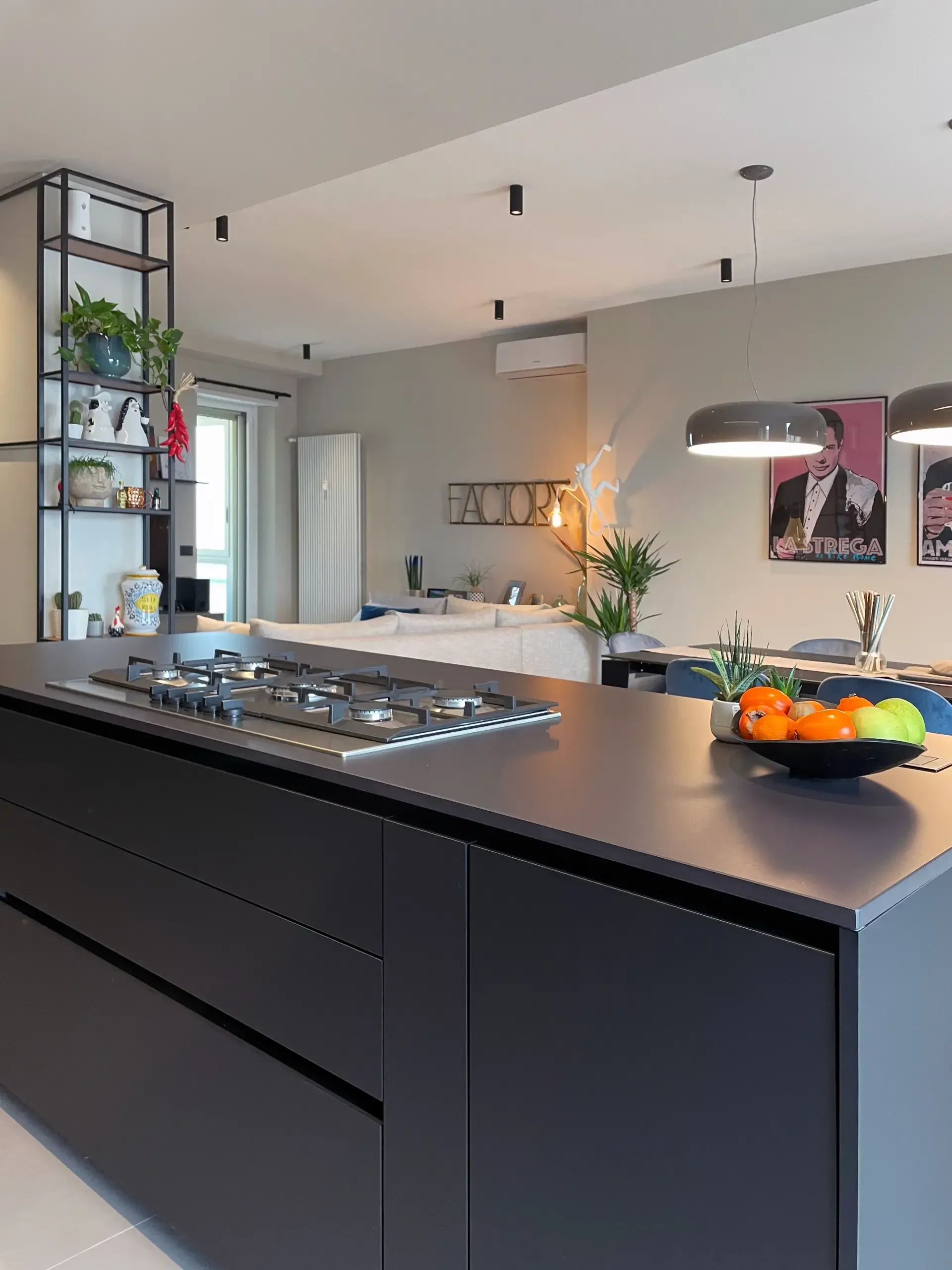 Cucina moderna con isola grigio scuro, piano cottura a gas e ripiani a vista con piante.