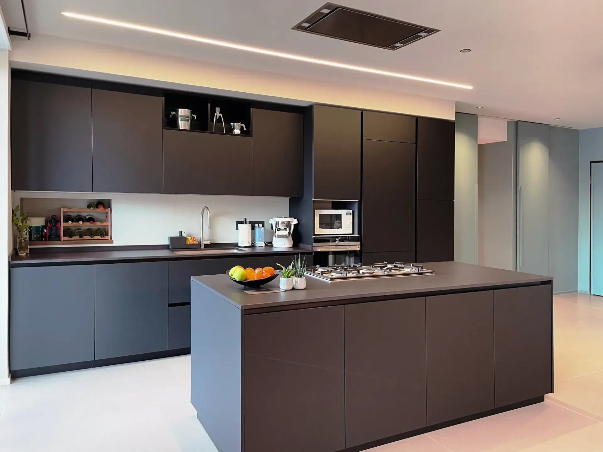 Moderna cucina grigio scuro con isola, elettrodomestici da incasso e illuminazione dall'alto.