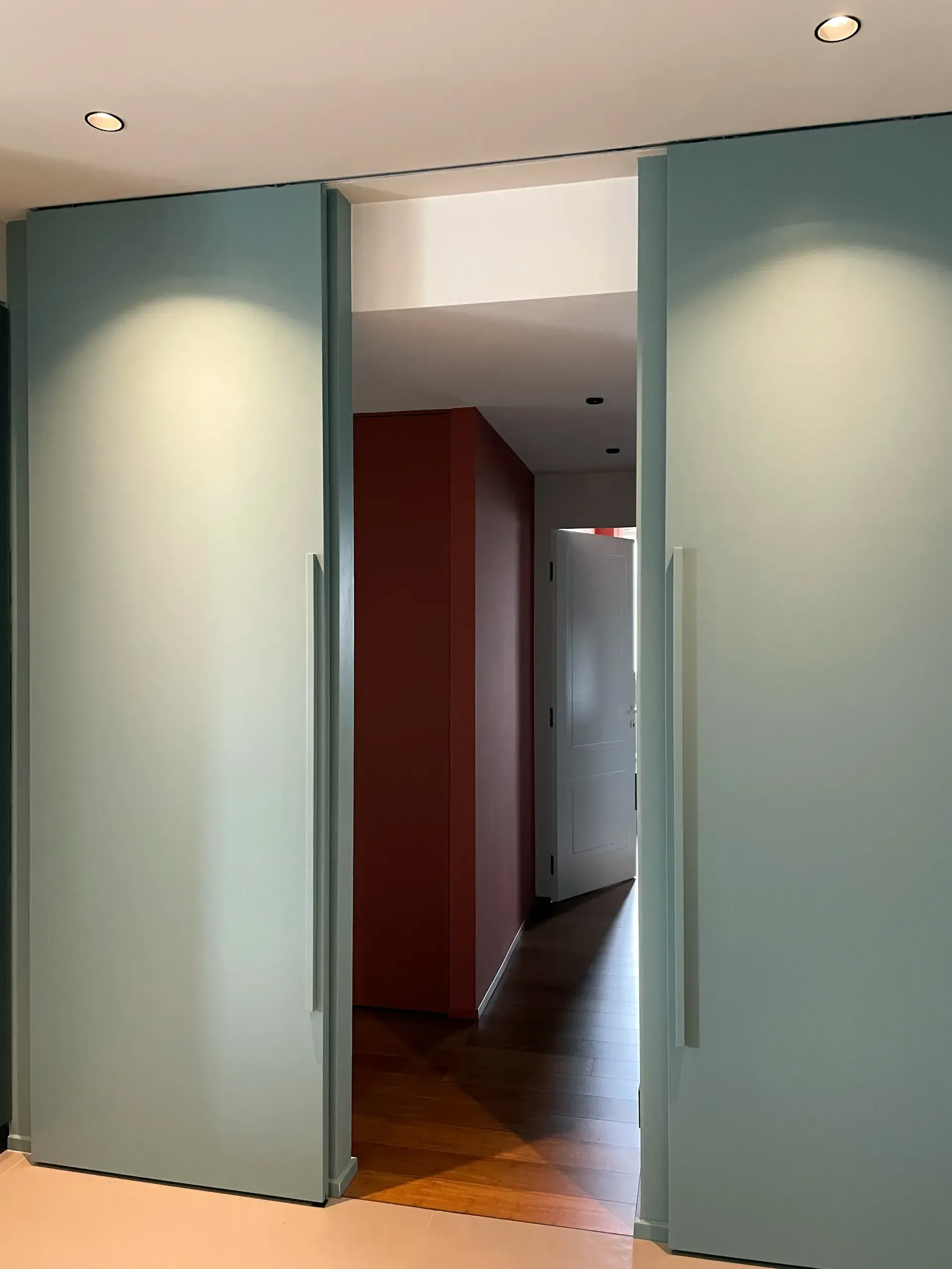 Due porte scorrevoli azzurre si aprono su un corridoio con una parete rossa e pavimenti in legno.