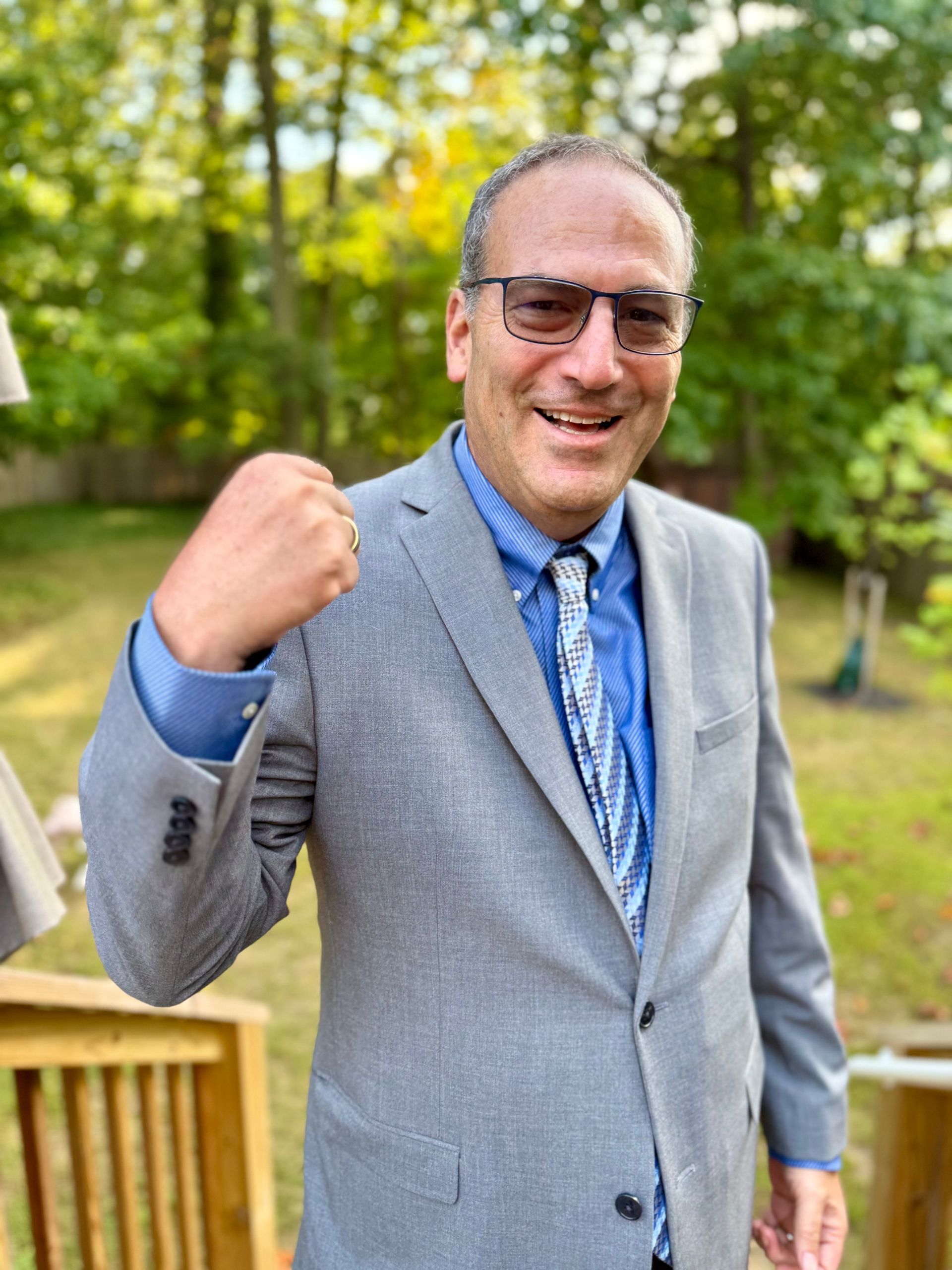 Man in a blue suit and colorful tie, smiling, standing in front of a blue background.