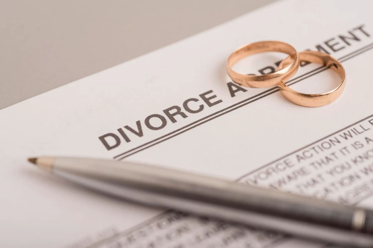 Divorce agreement document with gold wedding rings and a pen, symbolizing the end of a marriage.