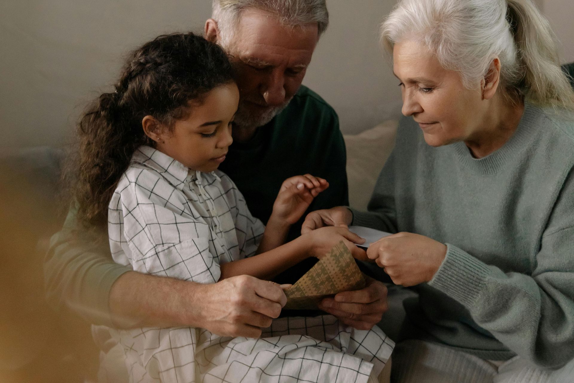 An elderly couple and a young girl look at something together. The girl holds the item as the woman examines it.