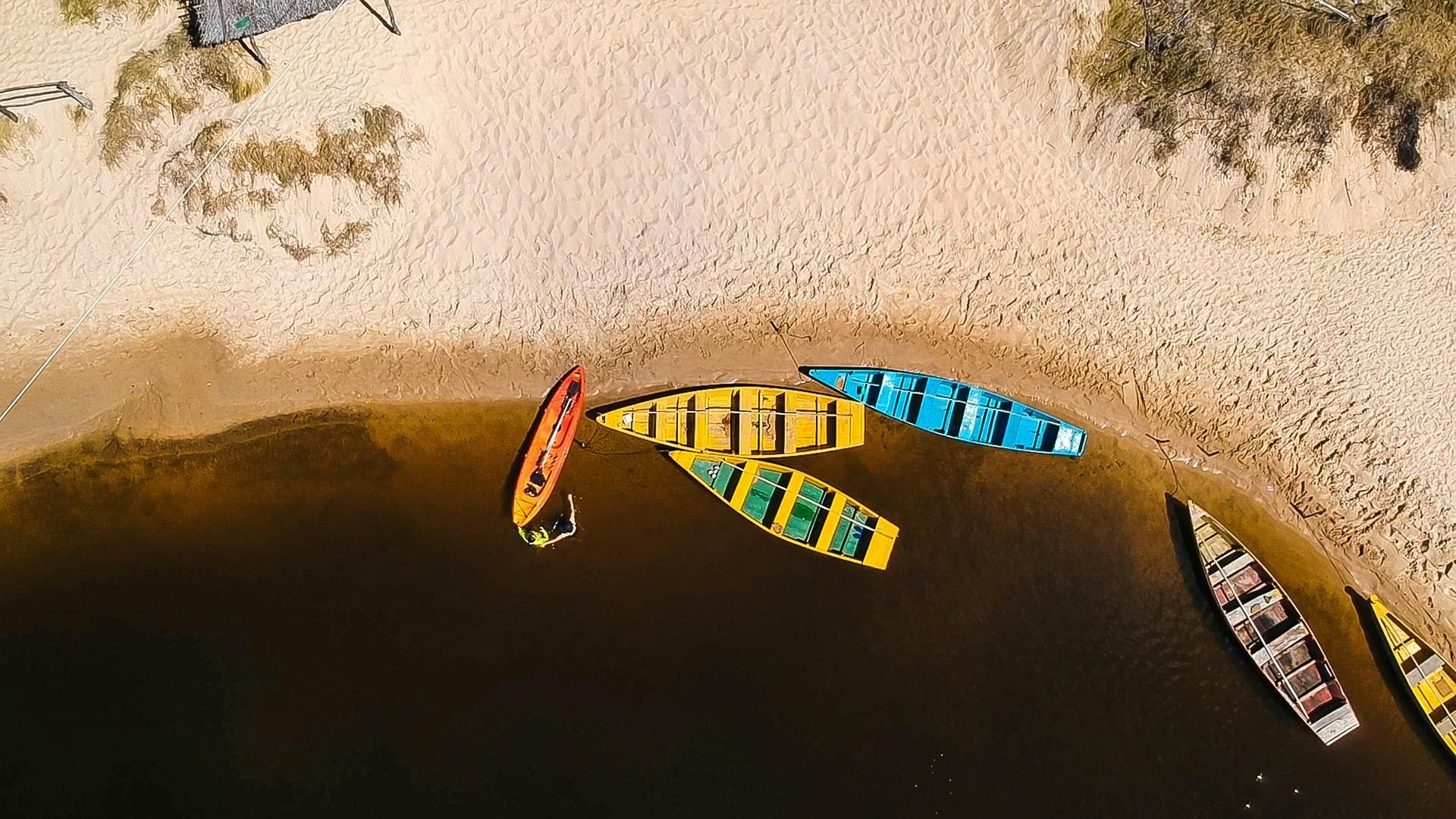 A group of colorful boats are sitting on the shore of a lake.