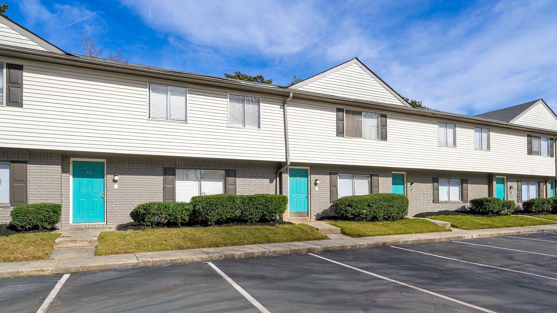Red brick apartment building with white columns and flags; green bushes and trees.