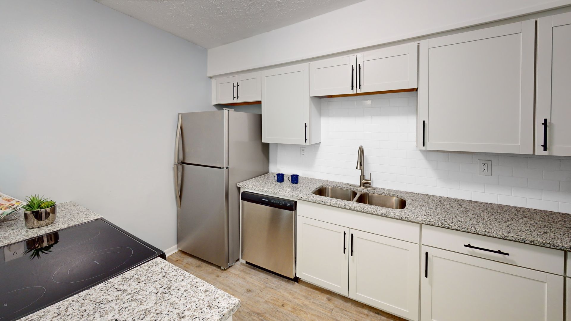 Kitchen with white cabinets, granite countertops, stainless steel appliances, and white subway tile backsplash.