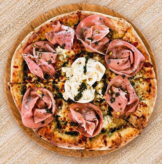 Pizza coberta com fatias de presunto dobradas e queijo derretido em uma tábua de madeira.