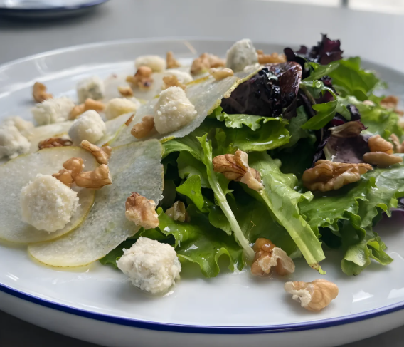 Salada de folhas verdes com fatias de pera, queijo esfarelado e nozes em um prato branco.
