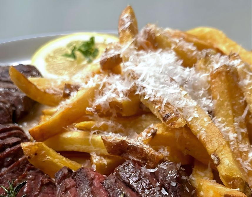 Massa coberta com queijo ralado, servida com carne grelhada e uma fatia de limão.
