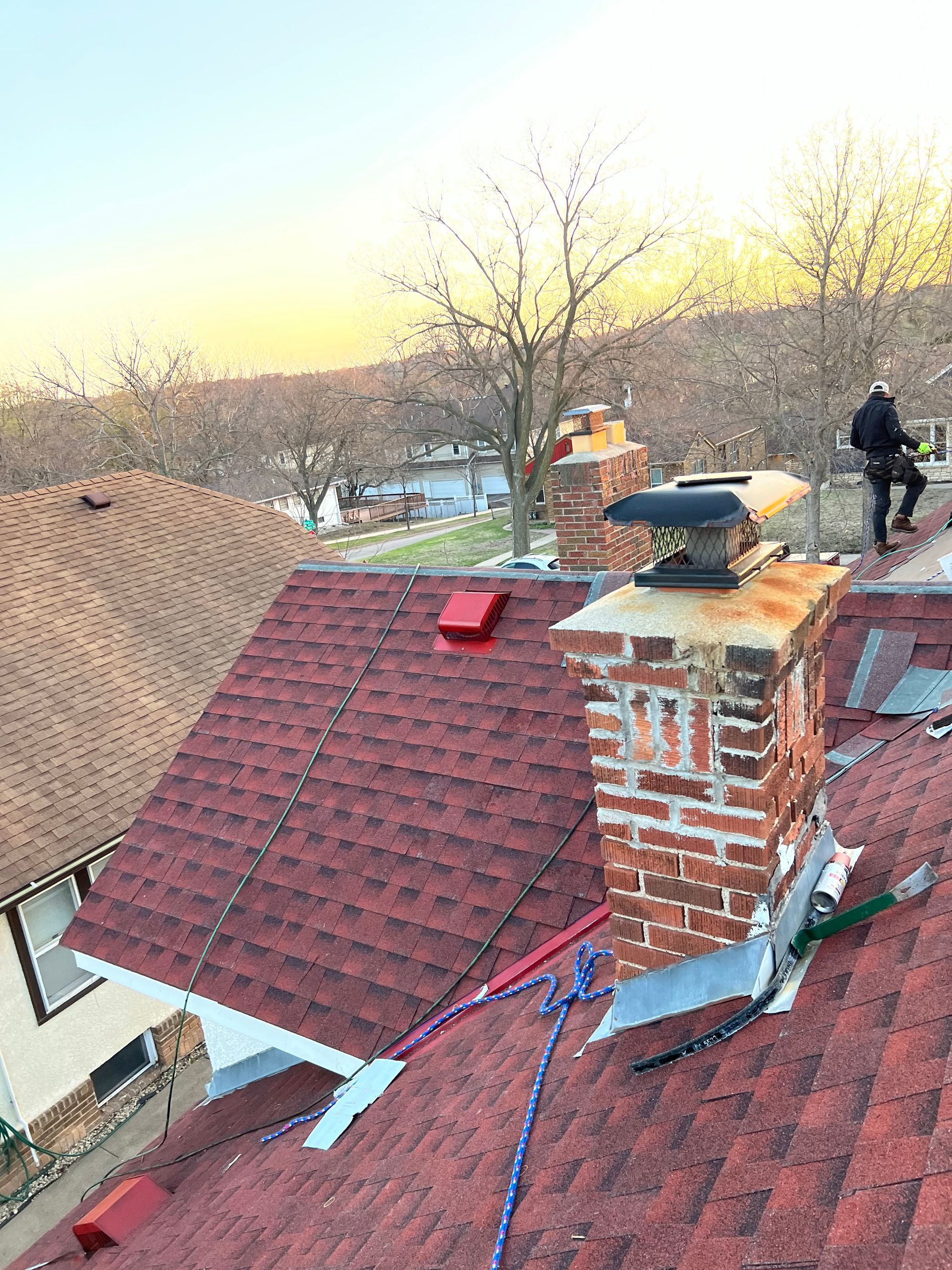 A man is standing on top of a roof next to a chimney.