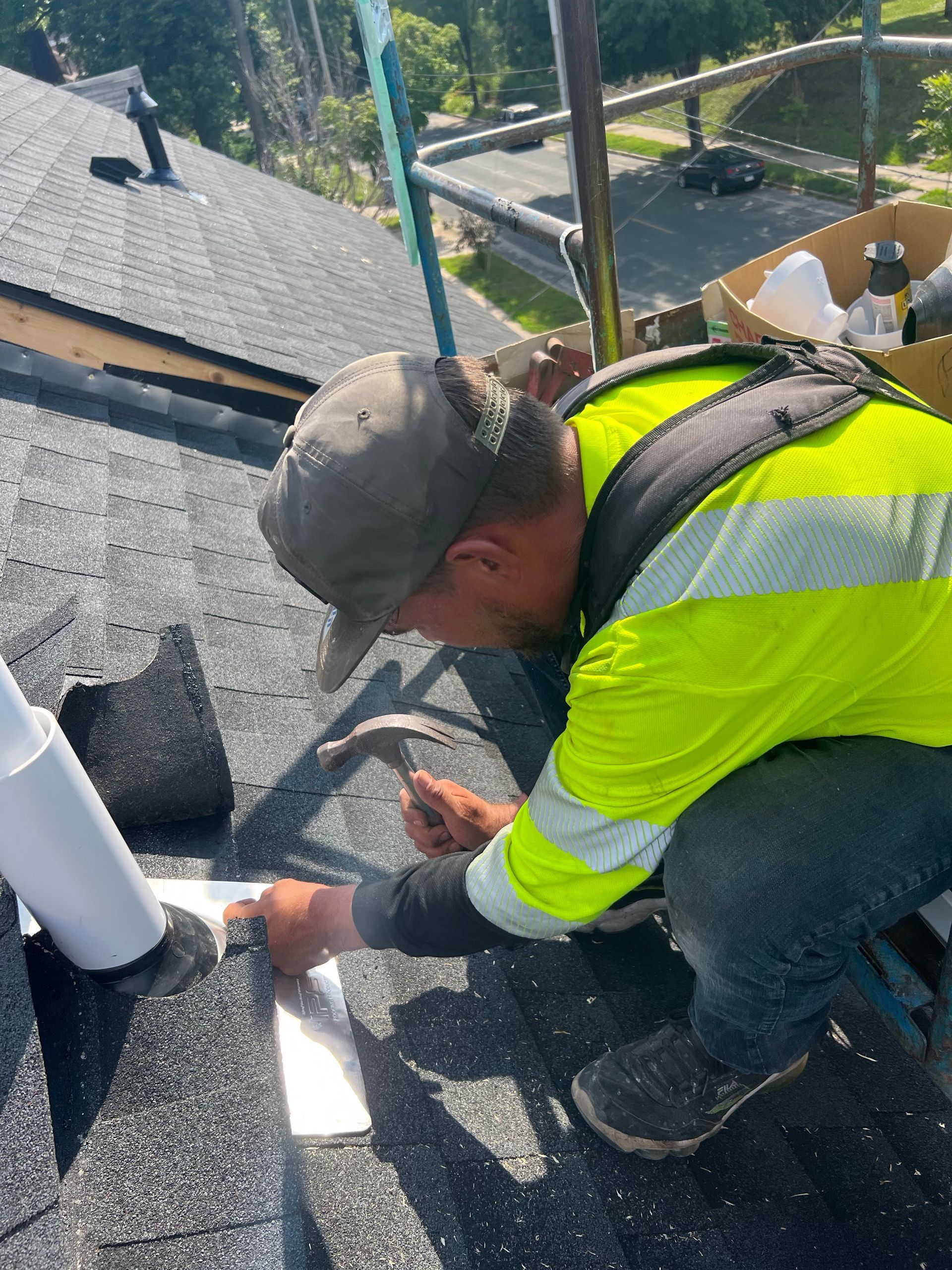 A man in a yellow vest is working on a roof with a hammer.