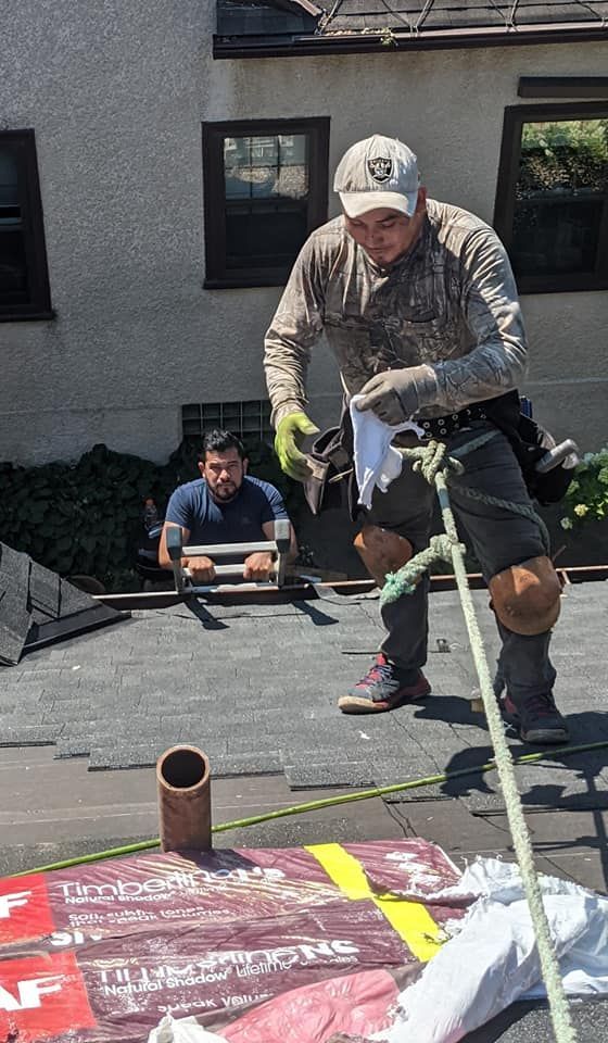 A man is standing on top of a roof holding a tool.