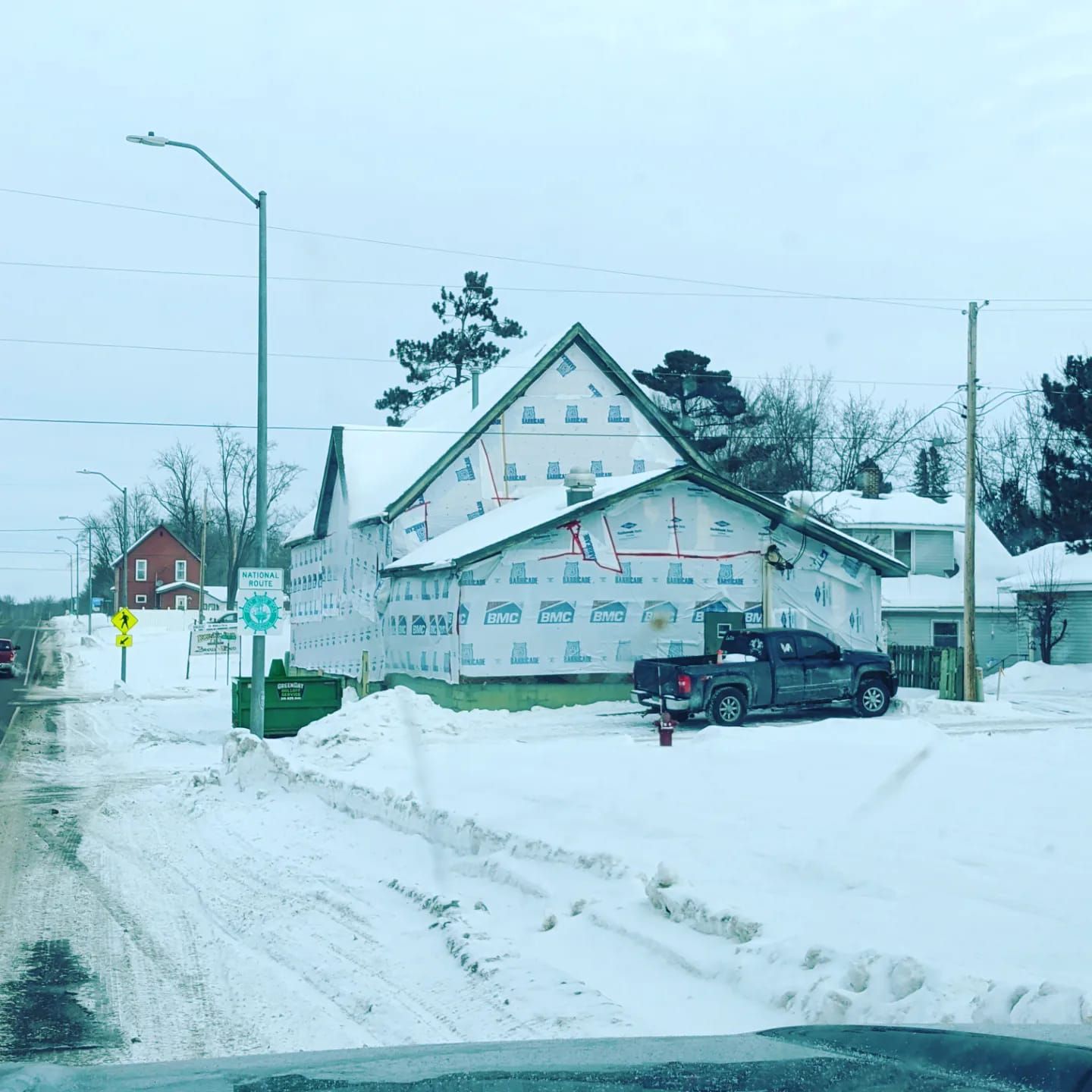 A truck is parked in front of a house that is being built in the snow.