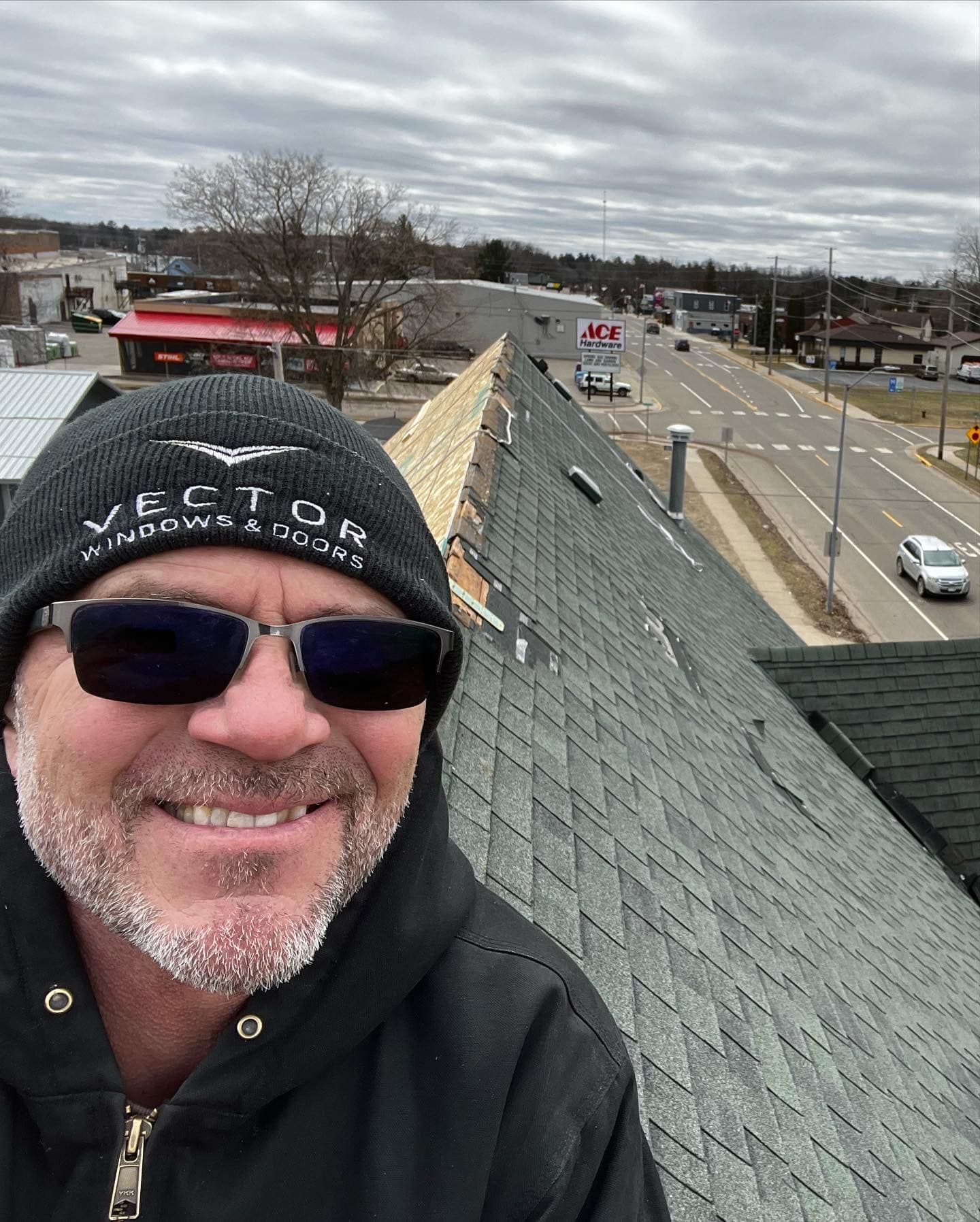 A man wearing sunglasses and a beanie is standing on top of a roof.