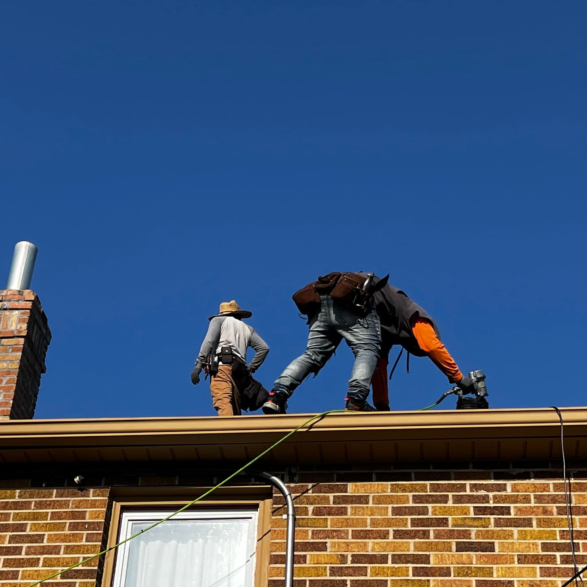 Two men are working on the roof of a brick building