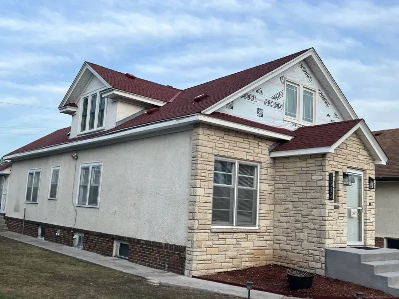A white house with a red roof and a stone facade